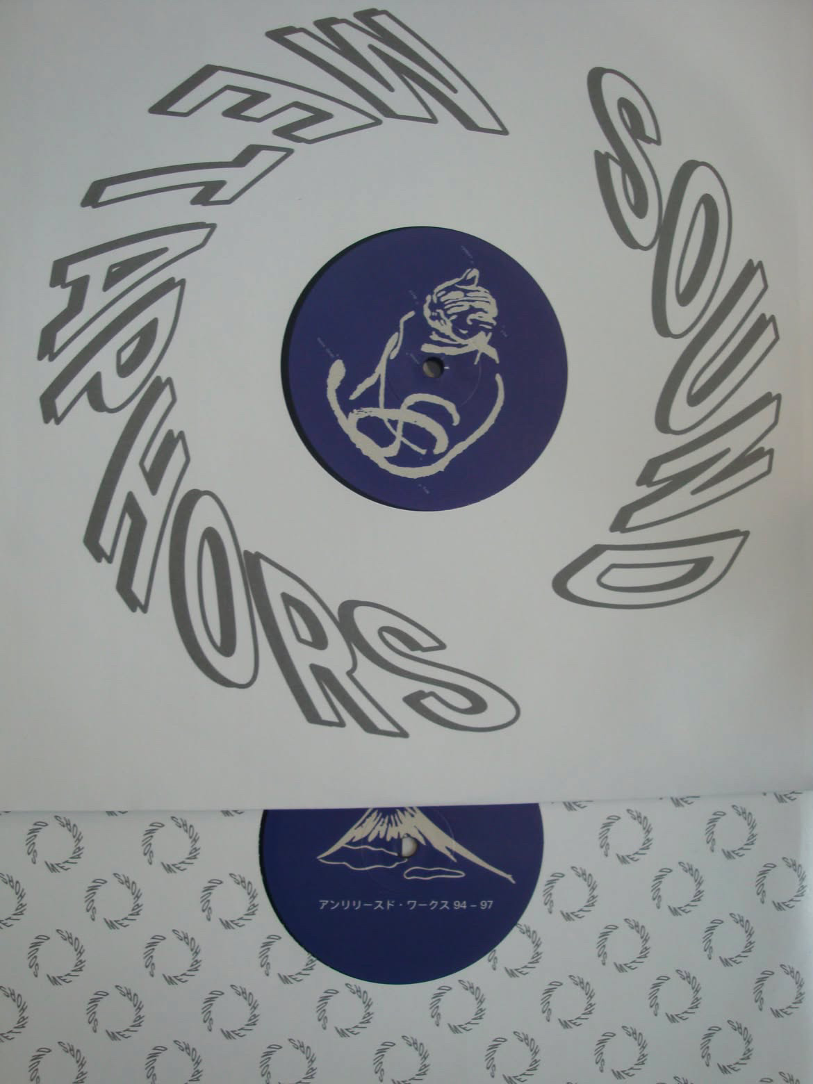 A vinyl record resting half out of its inner sleeve, printed with circular Sound Metaphors text; the record label carries a stylised Mount Fuji graphic above the Japanese title アンリリースド・ワークス 94-97.