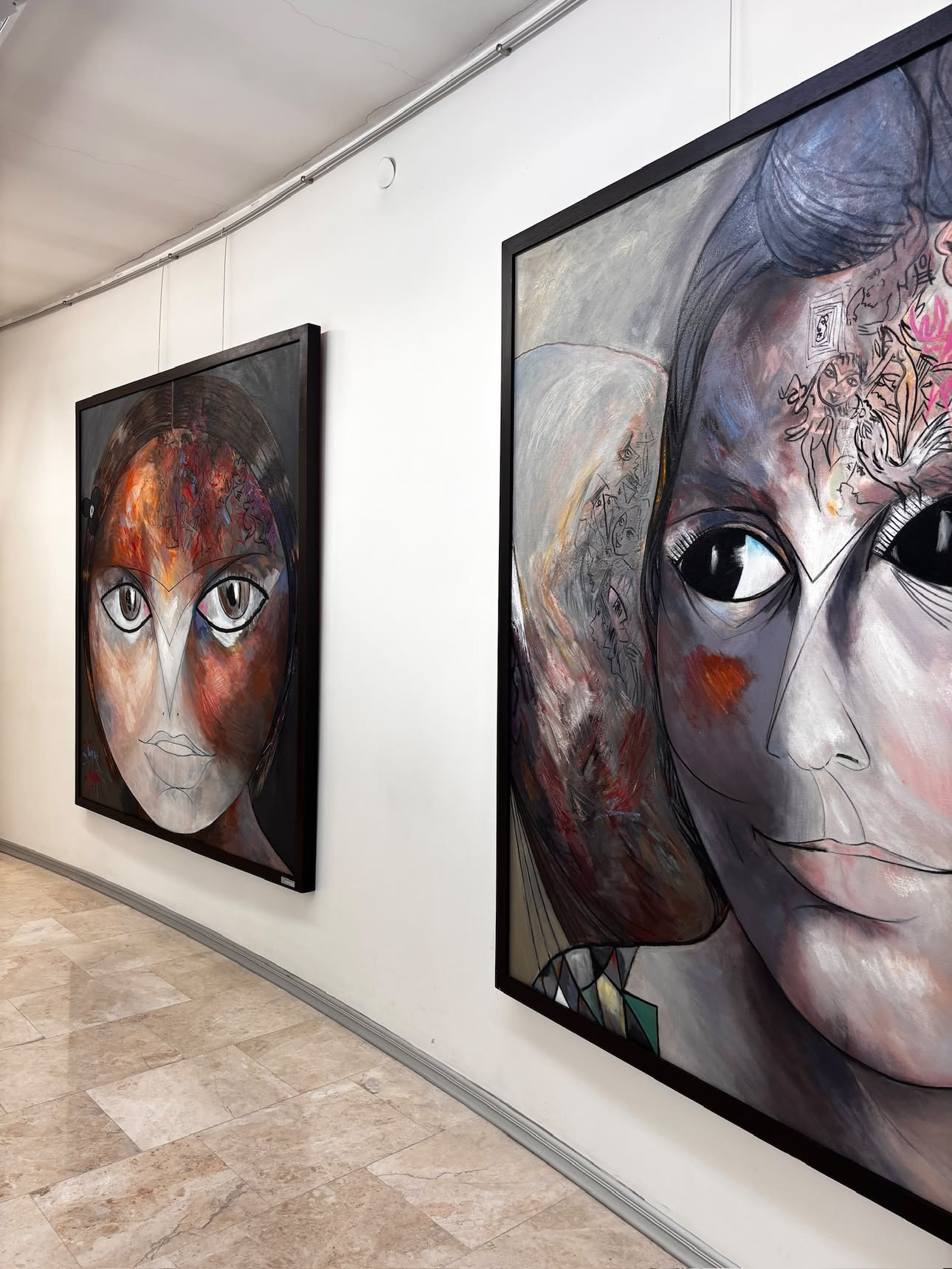 Two further large close-cropped face paintings, one in warm reddish-brown tones, one paler with dark hair and large dark eyes, hung at a corner of the gallery.