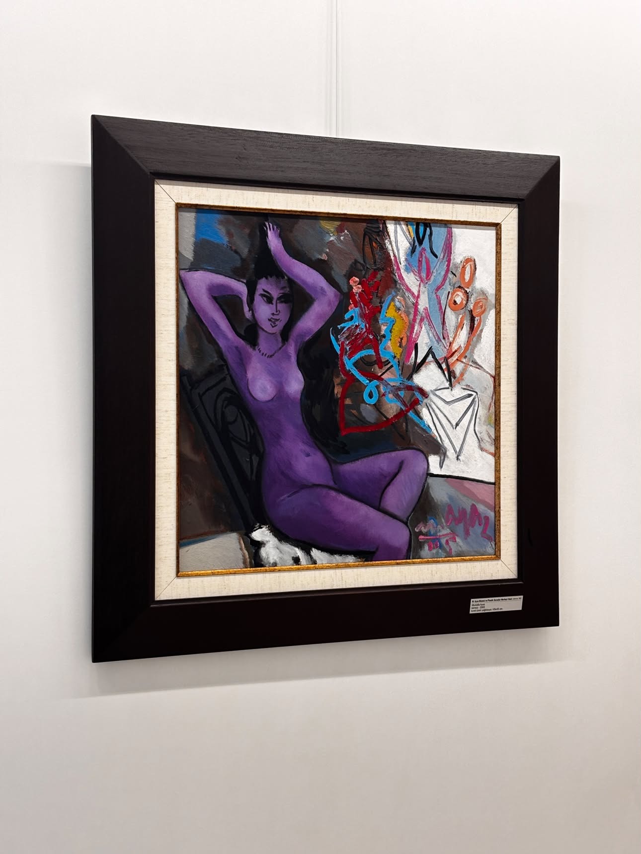 A painting of a purple-toned nude figure reclining with arms raised behind her head, smaller abstracted figures and marks in the background, in a dark wooden frame, a wall label legible at bottom right.