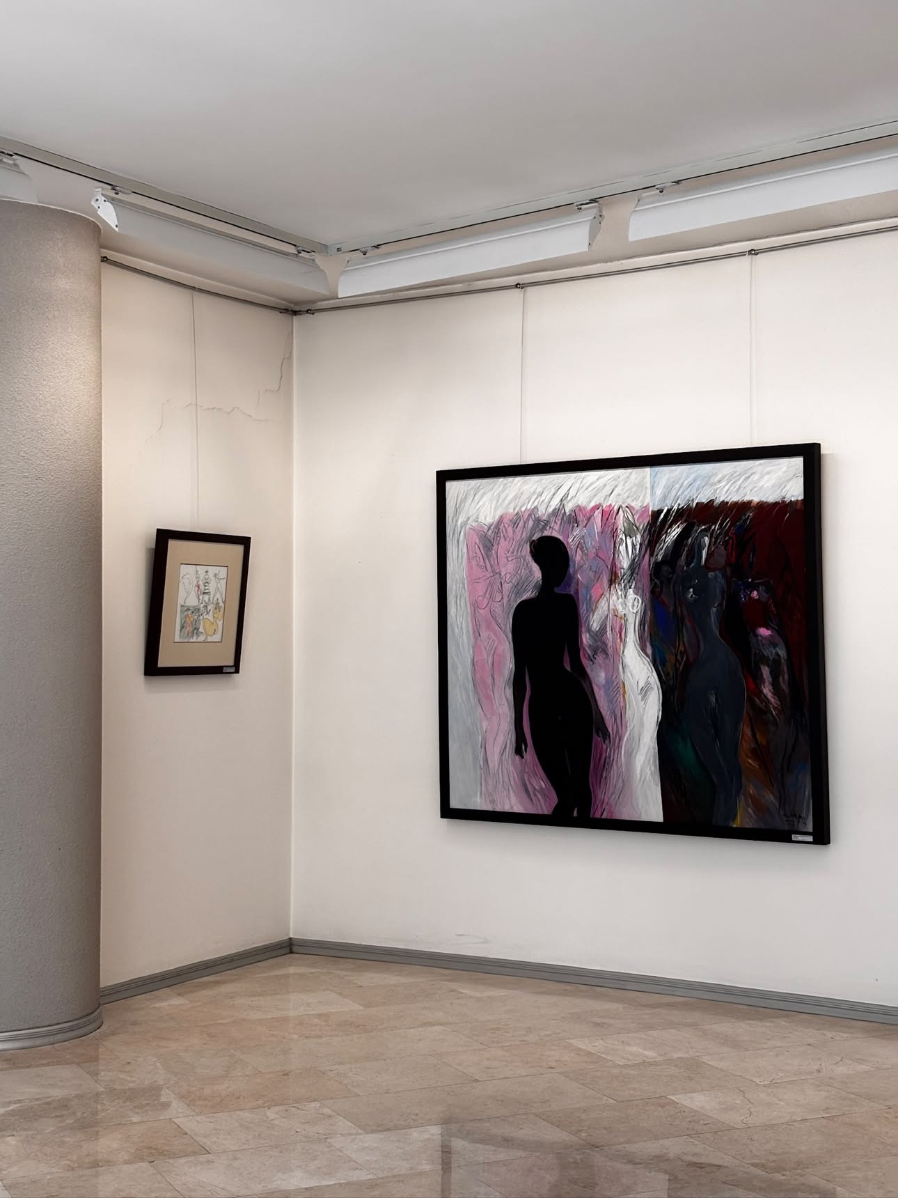 A gallery corner with a small framed drawing on the left wall and a larger painting on the right wall showing a dark silhouetted figure beside a paler ghostlike figure against a pink and grey ground, marble floor and a stone column in the foreground.