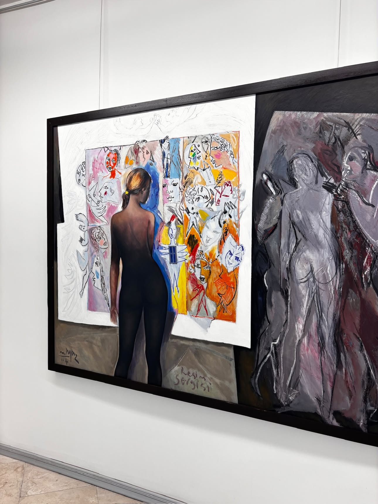 A large mixed-media composition of a dark, bare-backed figure seen from behind at its centre, standing before a collage of small sketched faces in pink, blue, orange and white, hung beside a grey-toned painting of two more figures embracing.