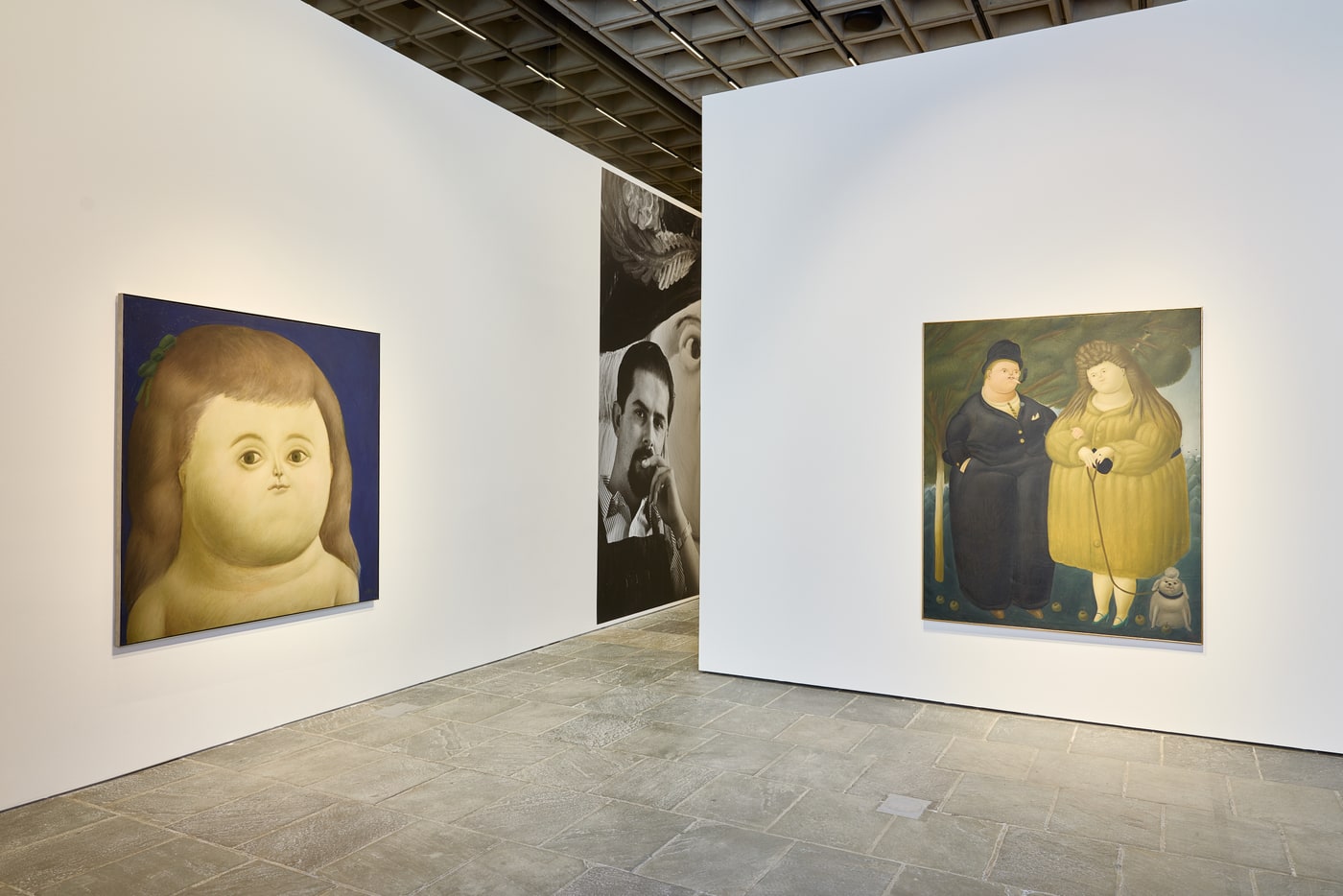 A large head of a girl with a green bow on a blue ground at left, a black-and-white photographic mural of a man smoking set beside an enlarged painted face in the centre, and a couple in a landscape walking a small white dog at right.