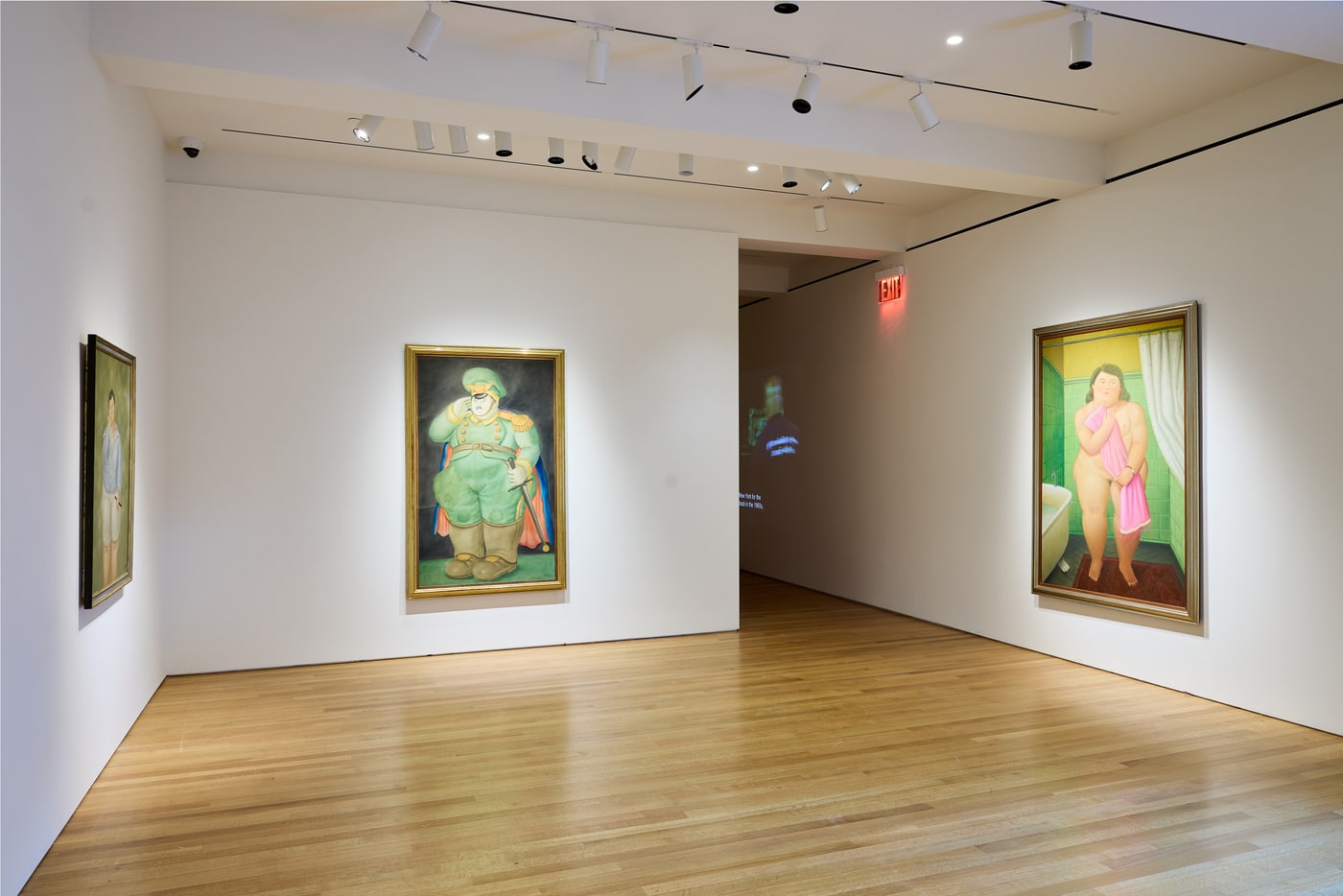 Pale wood floor. The edge of a boy's portrait at left, a military officer in green uniform saluting in the centre, and a woman in a green-tiled bathroom holding a pink towel at right, with a projection visible through the doorway.